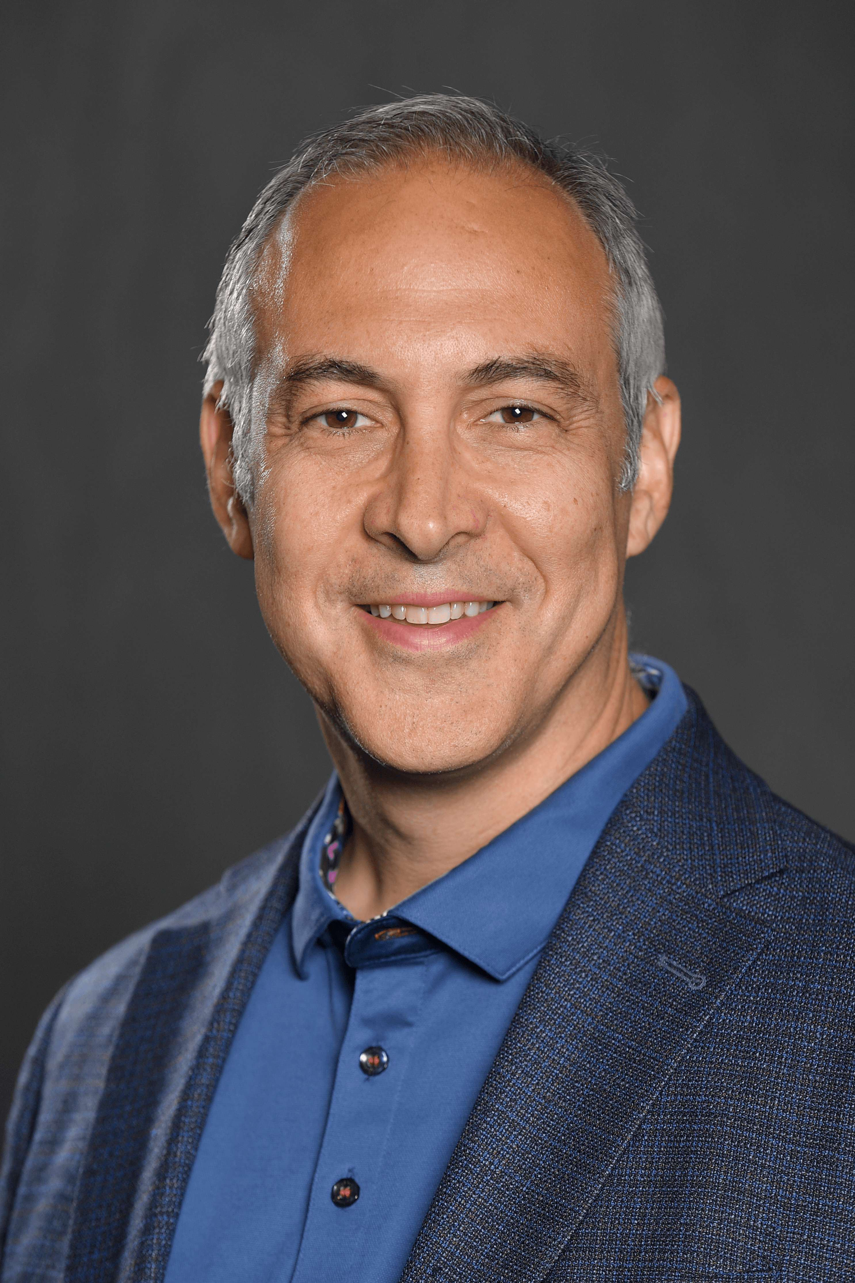Tony Pisani smiling in a head-and-shoulders portrait against a dark background.